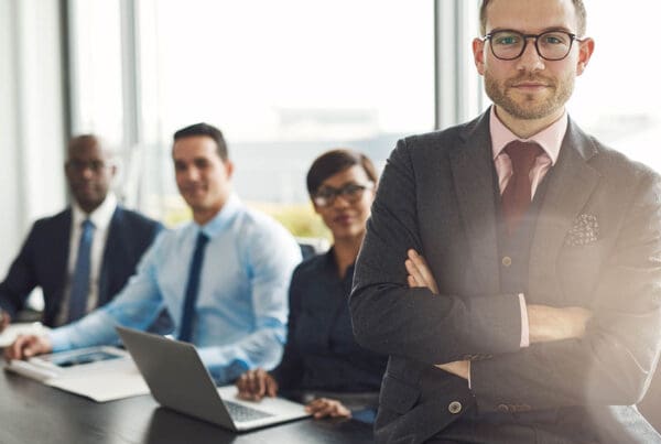 Meet Our Team - Professional and Welcoming Group at a Conference Table Faces the Camera, Team Leader Sitting on the Table with Arms Folded