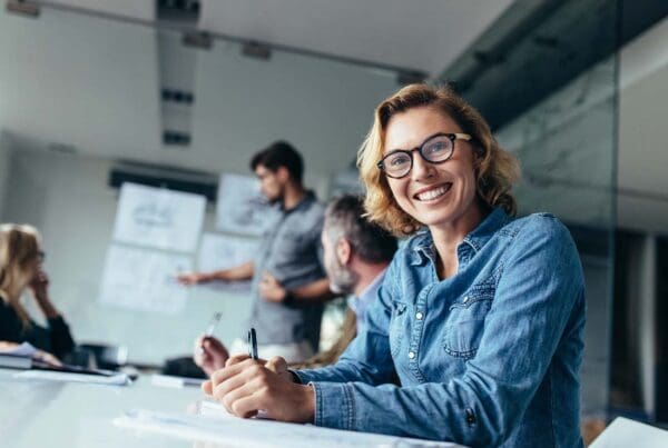 Commercial Bonds - Focus On a Young Woman Sitting in a Board Room during a Business Meeting and Smiling at the Camera with the Background Blurred