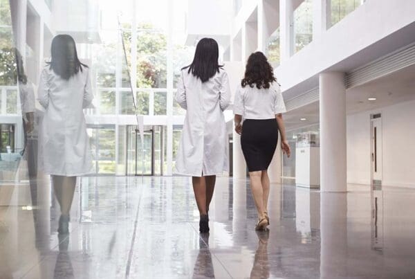 Group Hospital Insurance - Rear View of Doctors in a Modern Hospital as They Walk Away through the Hospital and Towards the Elevator