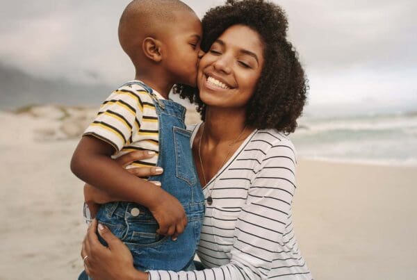 Individual Life Insurance - Young Son Kissing His Smiling Mother While Being Held at the Beach on a Cloudy Day