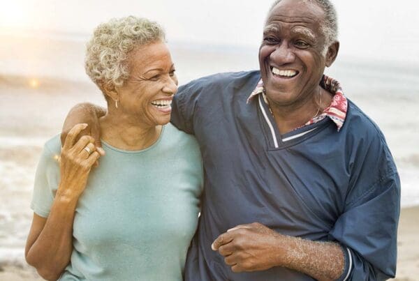 Individual Retirement Account - Senior Couple Laughing and Embracing One Another While Walking along the Beach at Sunset