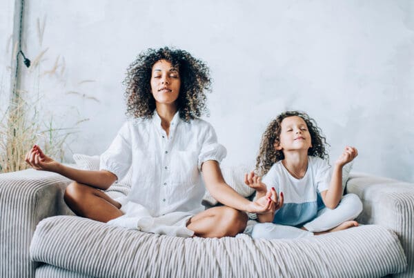 Wellness Benefit Plans - Mother and Daughter Meditating on the Coach in the Living Room