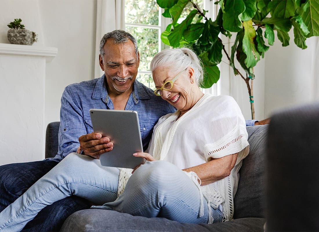 Service Center - Cheerful Elderly Couple Spending Time Together on the Sofa in the Living Room Looking at a Tablet